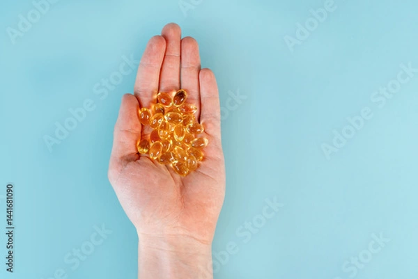 Obraz A man's hand holds omega-3 fish oil capsules on a blue table background. The concept of healthy nutrition and vitamins. Close up, point of view shot.