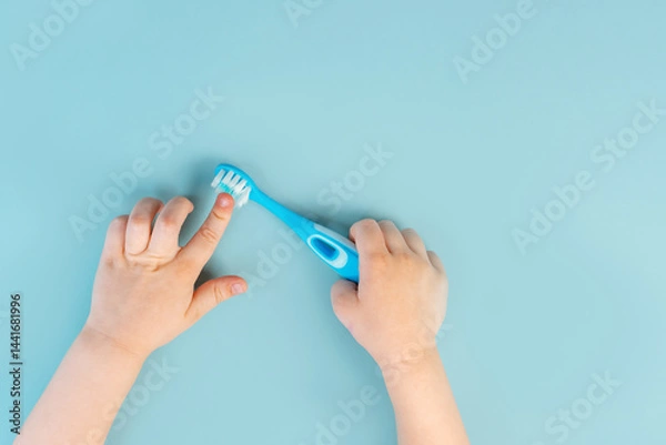 Obraz Little child's hands hold the toothbrush on the blue background. Close up, point of view shot. View from above. The concept of oral hygiene and dental cleaning.