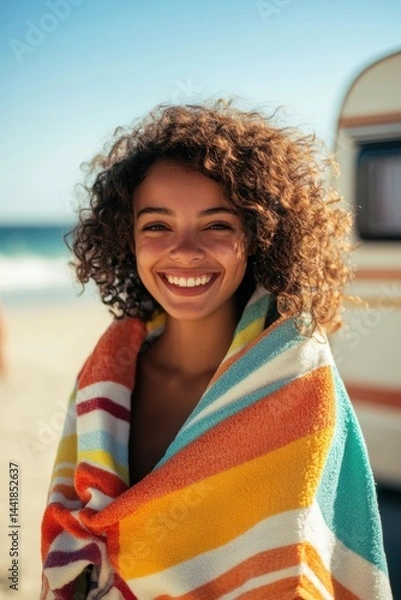 Fototapeta Smiling young woman wrapped in colorful beach towel posing at sunny seaside vacation destination enjoying summer fun and relaxation by ocean waves.
