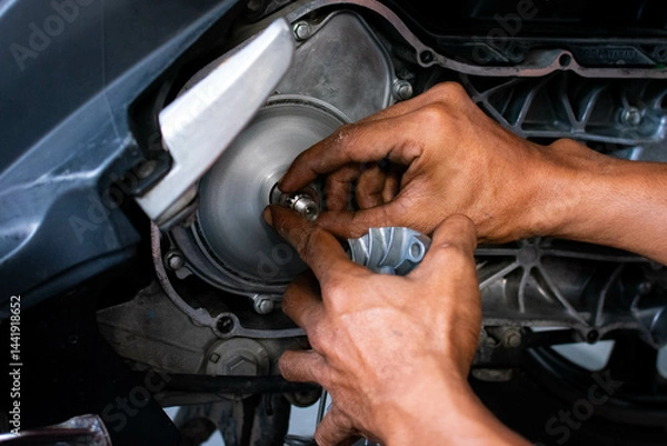 Fototapeta Close up of a mechanic's hands working on a scooter's CVT transmission system, focusing on the front pulley shaft during maintenance