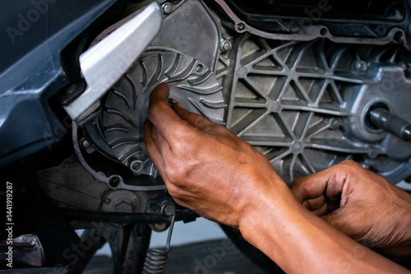 Fototapeta Close up of a mechanic's hands working on a scooter's CVT transmission system, focusing on the front pulley shaft during maintenance