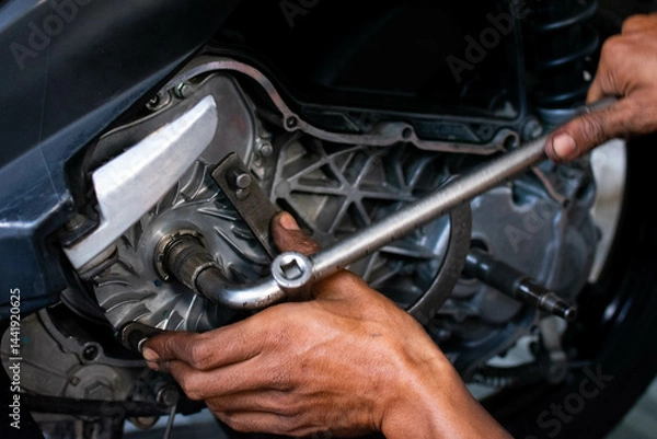 Fototapeta Close-up of a mechanic's hands working on a scooter's CVT transmission system, focusing on the front pulley shaft during maintenance