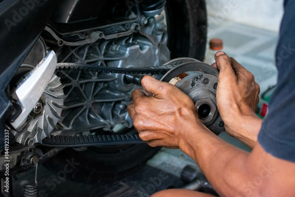 Fototapeta Close up of a mechanic’s hand adjusting the rear pulley axle of a scooter’s CVT transmission system during maintenance