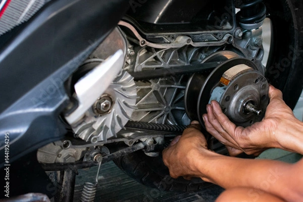 Fototapeta Close up of a mechanic’s hand adjusting the rear pulley axle of a scooter’s CVT transmission system during maintenance