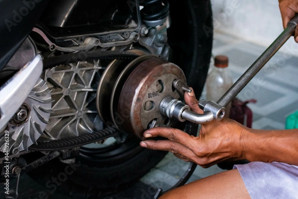 Fototapeta Close up of a mechanic’s hand adjusting the rear pulley axle of a scooter’s CVT transmission system during maintenance
