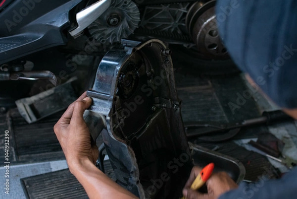Fototapeta Close-up of a mechanic’s hands cleaning a scooter’s CVT housing using a special cleaning liquid during routine maintenance