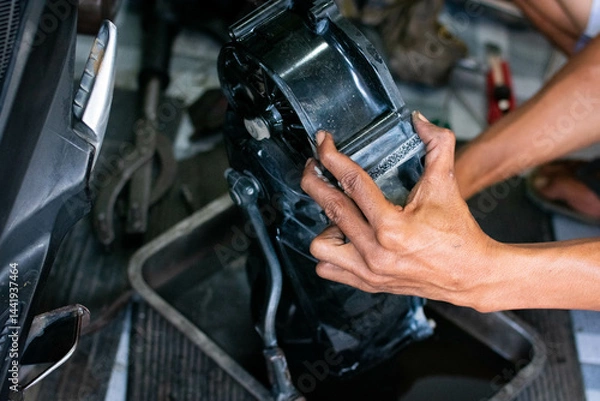 Fototapeta Close-up of a mechanic’s hands cleaning a scooter’s CVT housing using a special cleaning liquid during routine maintenance