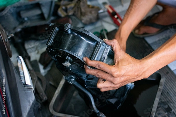 Fototapeta Close-up of a mechanic’s hands cleaning a scooter’s CVT housing using a special cleaning liquid during routine maintenance.