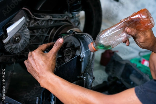 Fototapeta Close up of a mechanic’s hands cleaning a scooter’s CVT housing using a special cleaning liquid during routine maintenance