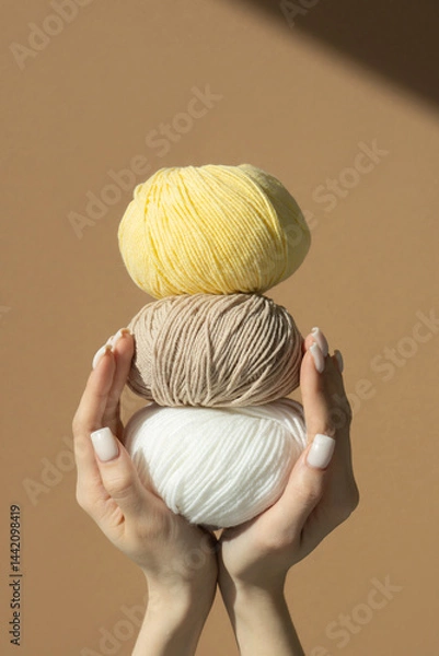 Obraz Three balls of knitting thread in women's hands on a brown insulated background in sunlight. Vertical frame.