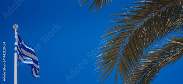 Fototapeta View of Greek flag waving in air serene Mediterranean vibe. beautiful Greek islands series, clear sky and palm leaves