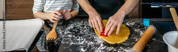 Fototapeta Banner of unrecognizable brother and sister cutting cookies from dough with various cookie cutters in a modern kitchen. Siblings making festive dessert together for a party at home.
