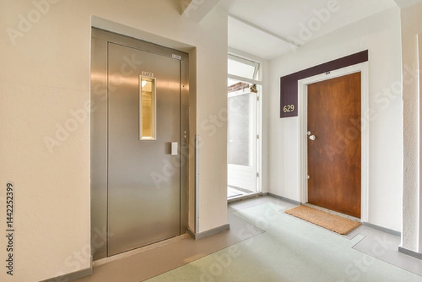 Fototapeta A sleek entrance hallway featuring an elevator and a wooden door, modern design elements, and smooth flooring create a welcoming atmosphere.