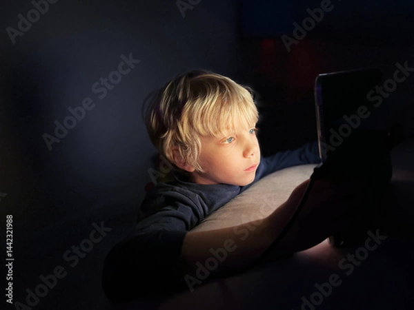 Obraz A Boy Watching Gadget Digital Device with Illuminated Screen in the Dark.  Impact on Child Development Concept, Screen Time.