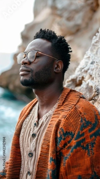 Fototapeta A man in glasses and sweater against a background of cliffs by the sea, great for fashion blogs, clothing ads, travel and lifestyle content.