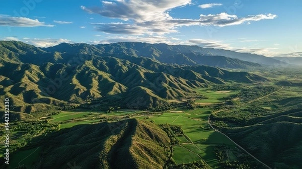 Fototapeta Forested mountain summits fading into sprawling green farmland, captured from above