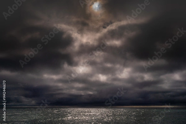 Fototapeta Sun between dark storm clouds over ocean. Dramatic seascape. Clouds and rain flurry over sea.