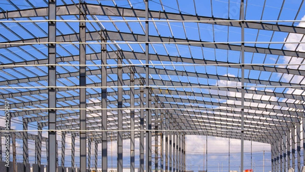 Fototapeta Geometric metal columns and roof beam structure of industry warehouse factory building in construction site against blue sky background