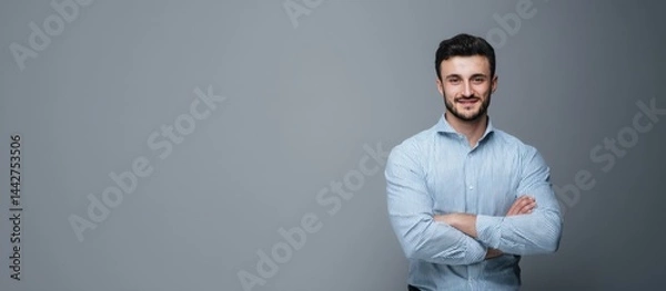 Obraz Young man in a striped shirt smiling confidently with arms crossed against a neutral background in a studio setting