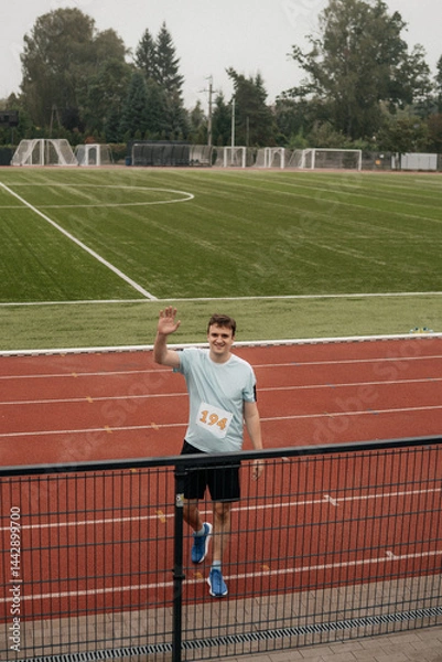 Obraz Runner at the stadium. A man takes part in a running competition. Male runner waving to his family