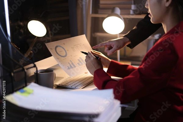 Fototapeta Business team working overtime analyzing financial data in office at night. Two business professional are working overtime in the office, analyzing financial data and discussing strategy for success.