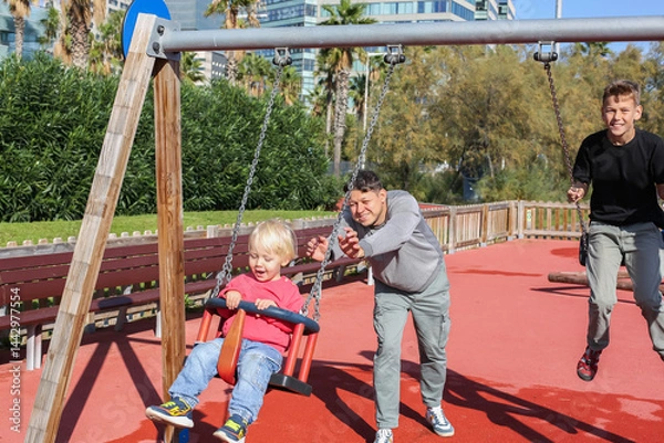 Fototapeta Father walking with teenager and toddler sons at a playground