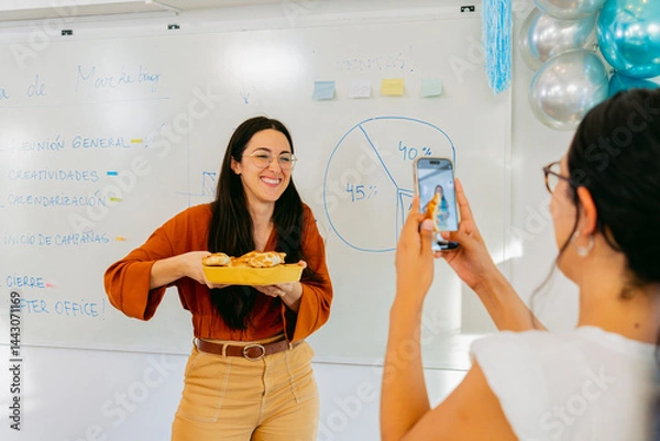 Obraz Young Latin woman takes a photo with phone for social media to her coworker with food in an after office