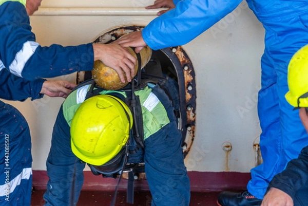 Fototapeta Crew member wearing breathing apparatus exits a narrow hatch after providing first aid during a man evacuation drill from a confined space on a merchant ship.