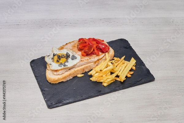 Obraz A delicious meal consisting of a sandwich, french fries, and an egg is served on a black plate. The sandwich is made with bread, ham, and cheese, while the fries are crispy and golden brown