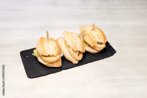 Obraz Three sandwiches on a black plate. The sandwiches are cut in half and have toothpicks in them