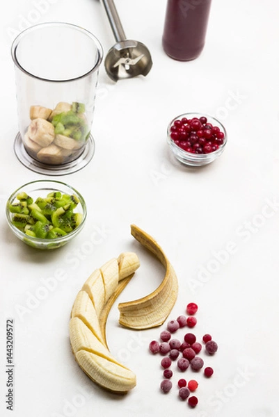 Obraz Frozen cranberries and sliced banana with peel on table. Cranberries and kiwi in bowls.