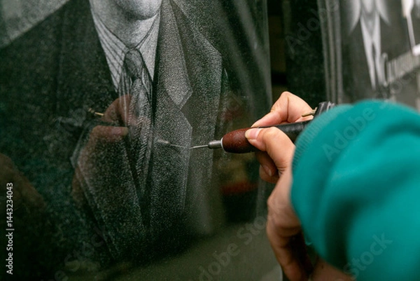Fototapeta The hand of a female artist who applies images to monuments by hand engraving.