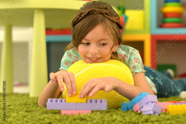 Fototapeta Portrait of cute girl playing with colorful plastic blocks in room