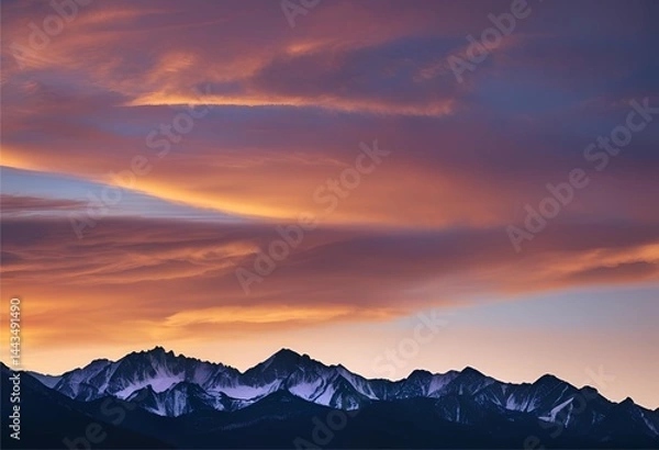 Fototapeta The sky glows warmly at sunset, casting soft light over the dark-colored mountain peaks.

