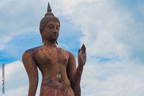 Fototapeta Buddha statue standing with cloudy sky background in Sukhothai historical park, Sukhothai province, Thailand