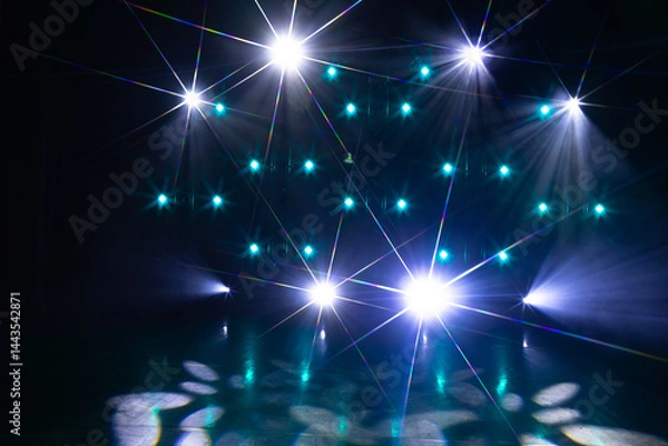 Fototapeta A vibrant stage setup features intense white spotlights and teal-blue LED lights arranged in a grid, casting dramatic starburst flares and patterns on the floor.