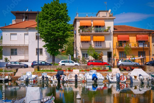 Fototapeta Rimini harbor seascape with moored boats and ships and traditional architecture along the Marecchia River in Rimini, Emilia-Romagna, Italy, blending coastal life with historic charm