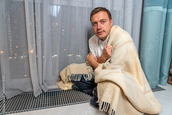 Obraz A Cold Night In The City: Man wrapped in blanket near window, feeling cold with city lights