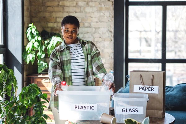 Obraz Young African American woman is doing garbage waste sorting at home. Concept of sustainable lifestyle, daily routine to protect planet from pollution, domestic life, simple actions for environment