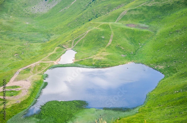 Fototapeta Breathtaking view of rolling green hills, serene high-altitude blue Dogyaska lake, under cloudy sky, showcasing nature's beauty. Svydovets ridge, Carpathian Mountains, Ukraine