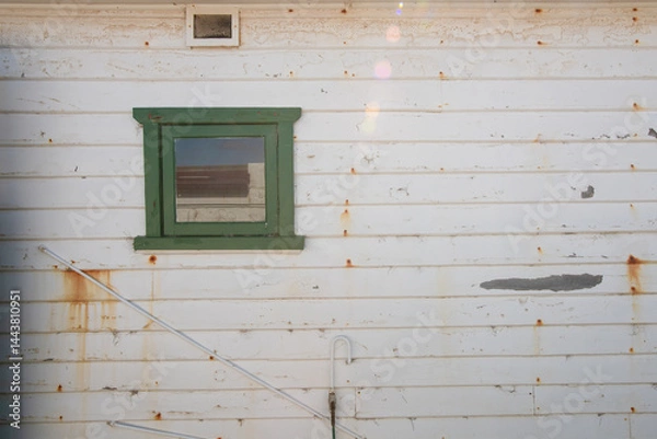 Obraz a wooden wall on a building with a small green painted window, chipped paint and rust stains add to the weathered look