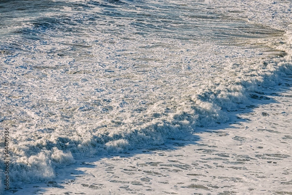 Fototapeta Waves crashing on the shore at sunset near a serene beach