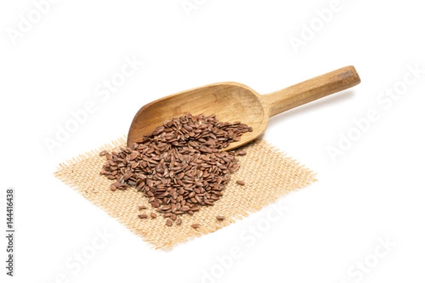 Fototapeta Linseed and a slanted wooden spoon on a piece of sack cloth with white background