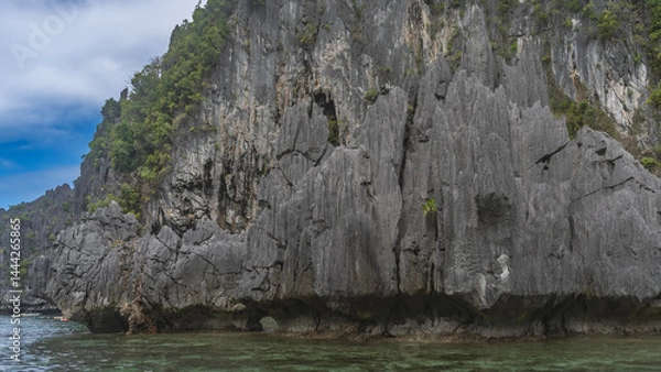 Fototapeta Picturesque cliffs surround the emerald lagoon. There is green tropical vegetation on the steep, furrowed slopes. Blue sky, clouds. Philippines. Palawan. Bacuit bay