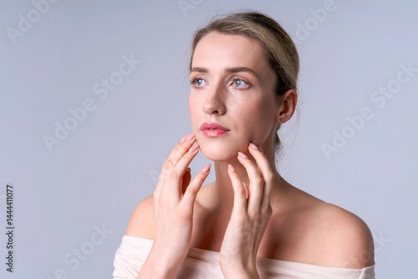 Fototapeta A woman touches her face with care, emphasizing the importance of preventing age-related changes and daily skin care