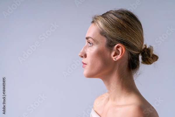 Fototapeta Profile of a young woman with smooth skin and well-groomed hair tied in a bun on a light background. Ideal for cosmetology, skin care and beauty concepts