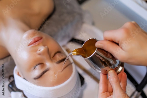 Obraz A woman is receiving a Japanese head spa treatment at a beauty salon. The therapist gently pours water, liquid onto her forehead to enhance relaxation of a scalp. Atmosphere promotes stress relief