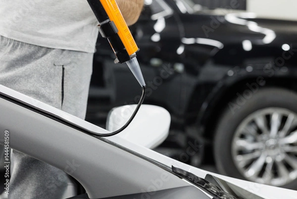 Fototapeta Worker applies special adhesive sealant to windscreen before installation on auto.