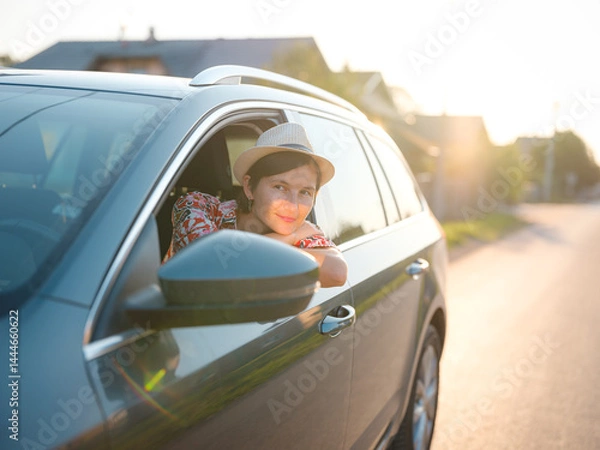 Fototapeta Traveler woman in red ethnic dress and hat drives car through scenic countryside of Croatia in summer. Surrounded by lush fields and forests, she enjoys peaceful and adventurous road trip
