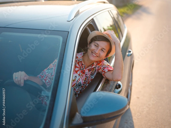 Fototapeta Traveler woman in red ethnic dress and hat drives car through scenic countryside of Croatia in summer. Surrounded by lush fields and forests, she enjoys peaceful and adventurous road trip